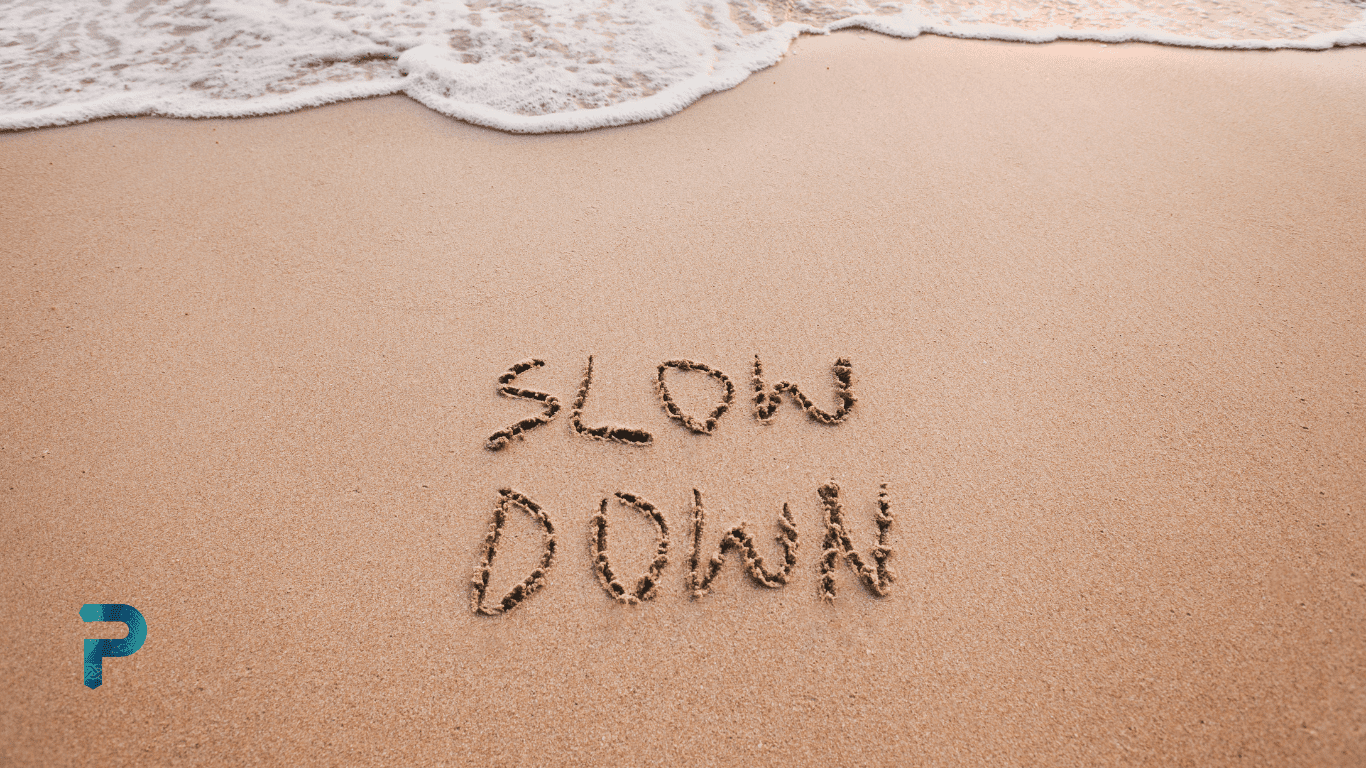 waves on sandy beach with slow down written in sand